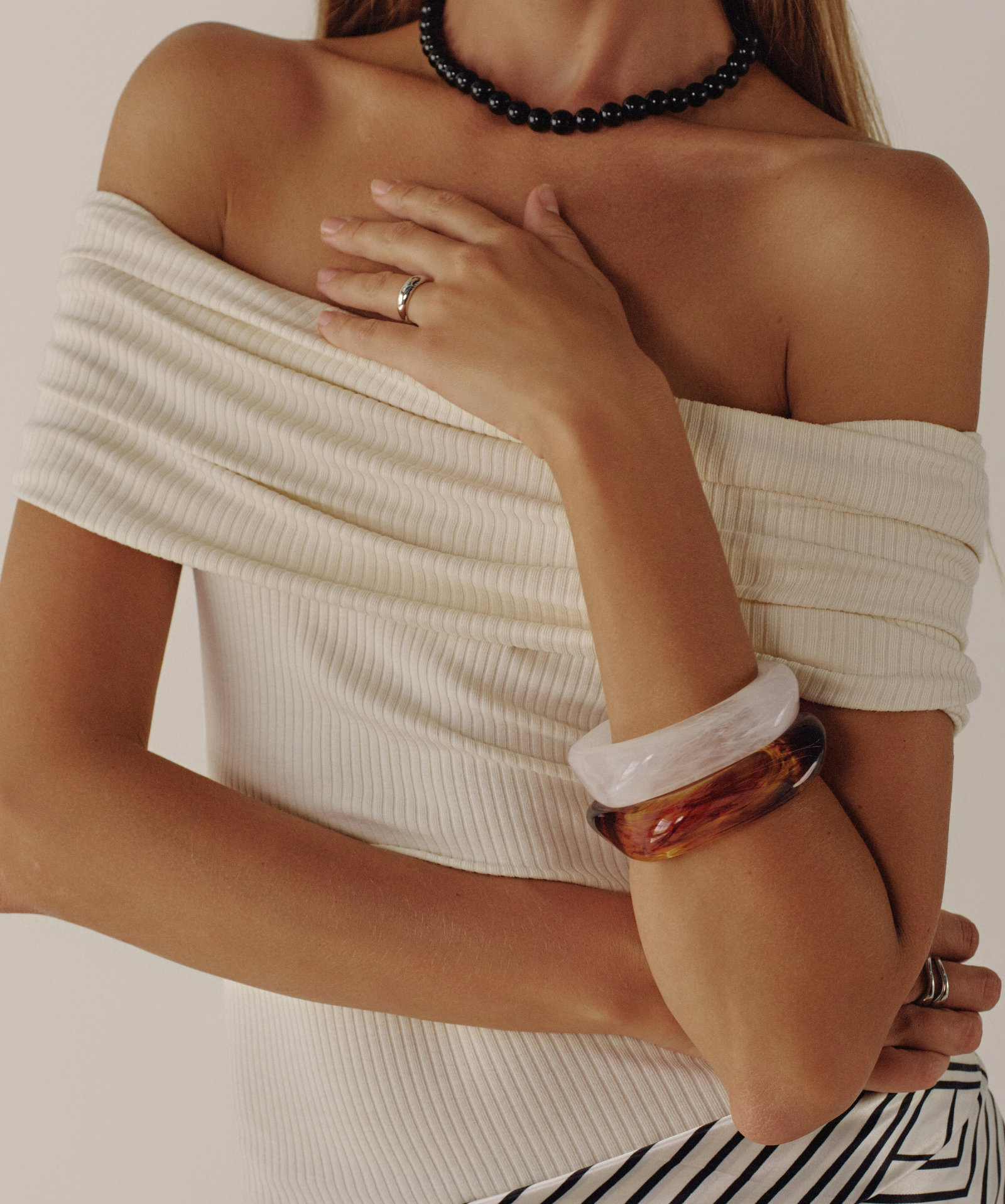 Woman wearing a white off-shoulder top and striped pants with jewelry on a neutral background