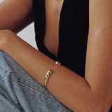 Person wearing gold jewelry with a black top and gray pants on a neutral background