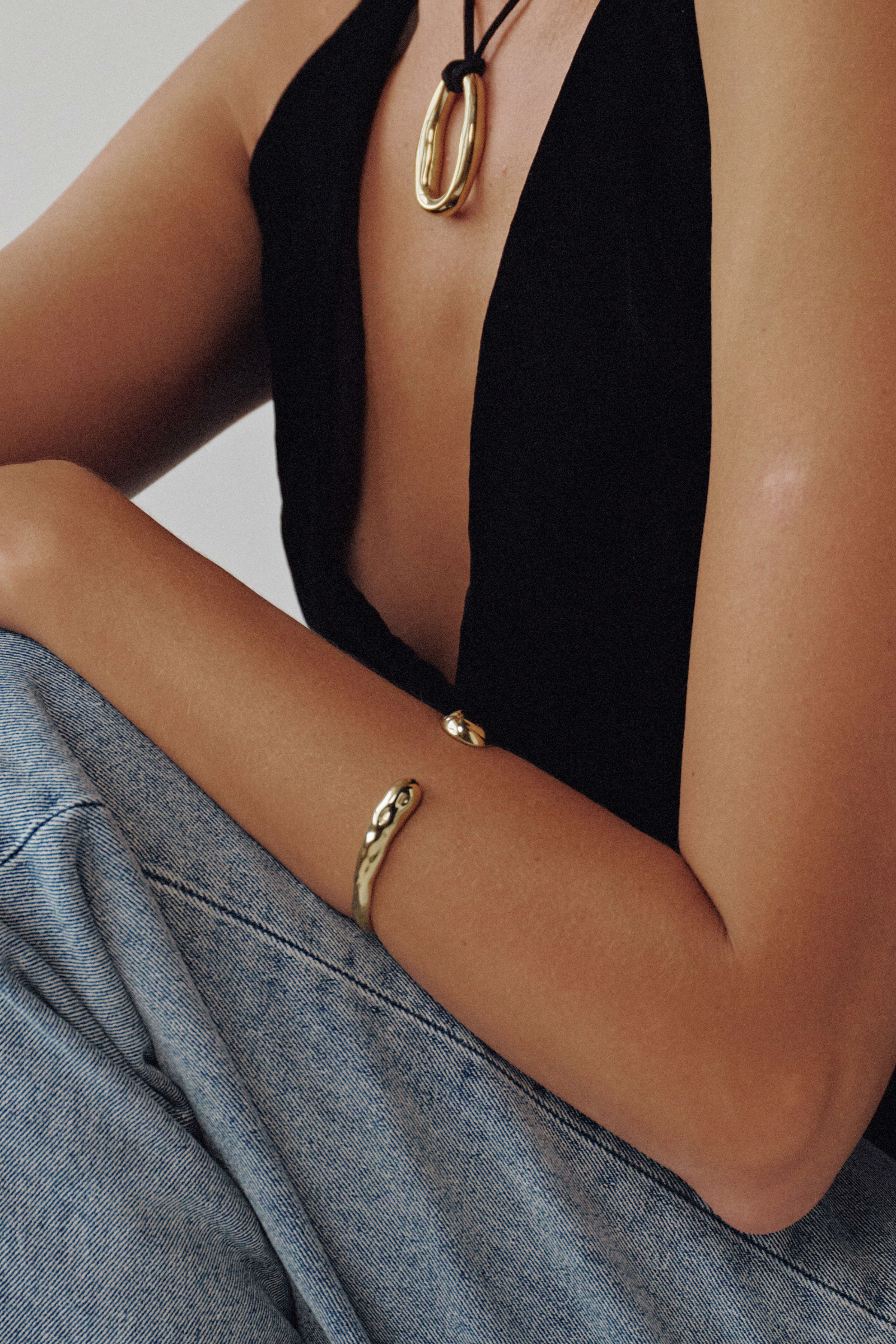 Person wearing gold jewelry with a black top and gray pants on a neutral background