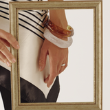 Person holding a gold-framed mirror with reflection showing a striped shirt and bangles.
