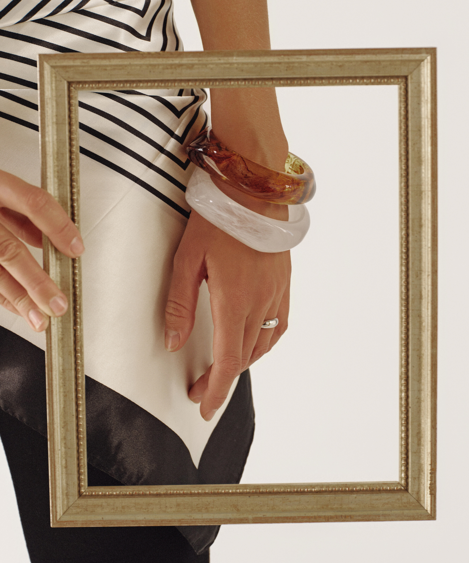 Person holding a gold-framed mirror with reflection showing a striped shirt and bangles.