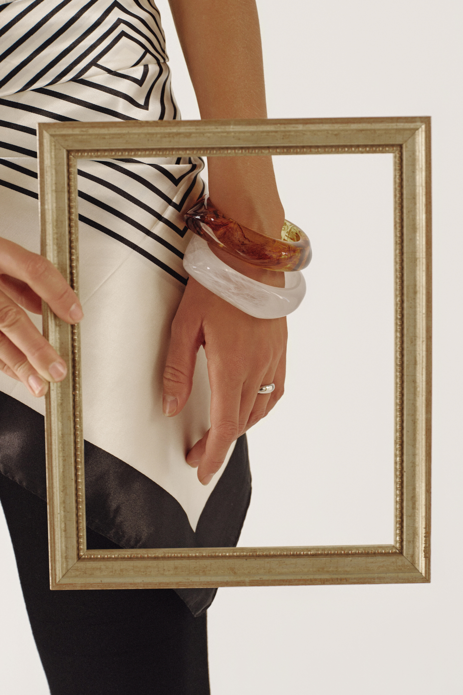 Person holding a gold-framed mirror with reflection showing a striped shirt and bangles.
