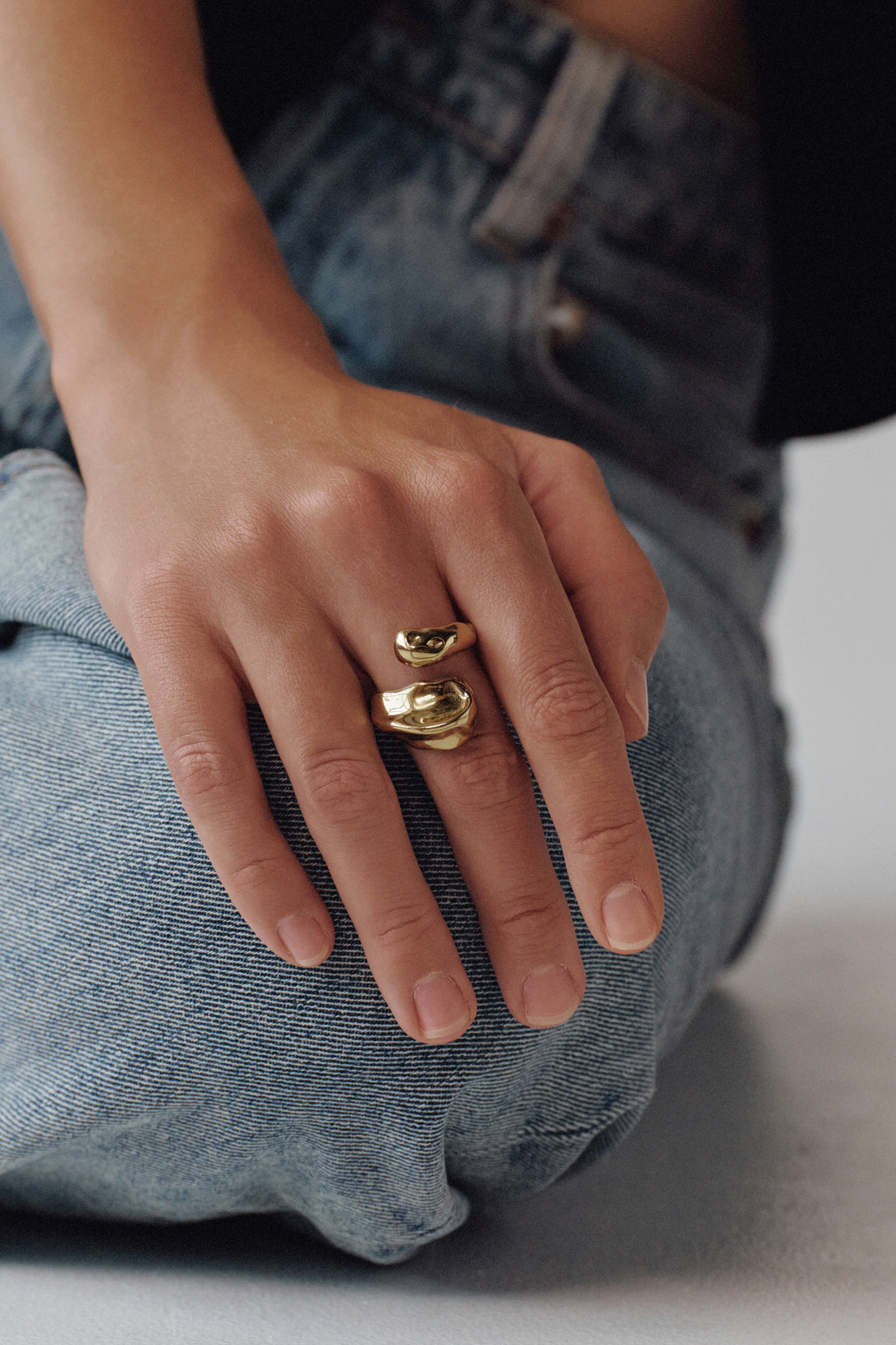 Hand wearing a gold ring on a neutral background