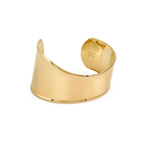 A wide, polished gold statement cuff bracelet featuring a smooth, asymmetrical wavy design and an open back, with the letters "TC" subtly engraved on the inner curve, isolated on a white background.