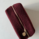 A dark red travel pouch with a gold zipper and a gold pendant with an engraved butterfly design and Twenty Compass logo.