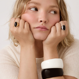 Close-up of model wearing gold and silver oval black stone rings with black and white cuff bracelets.