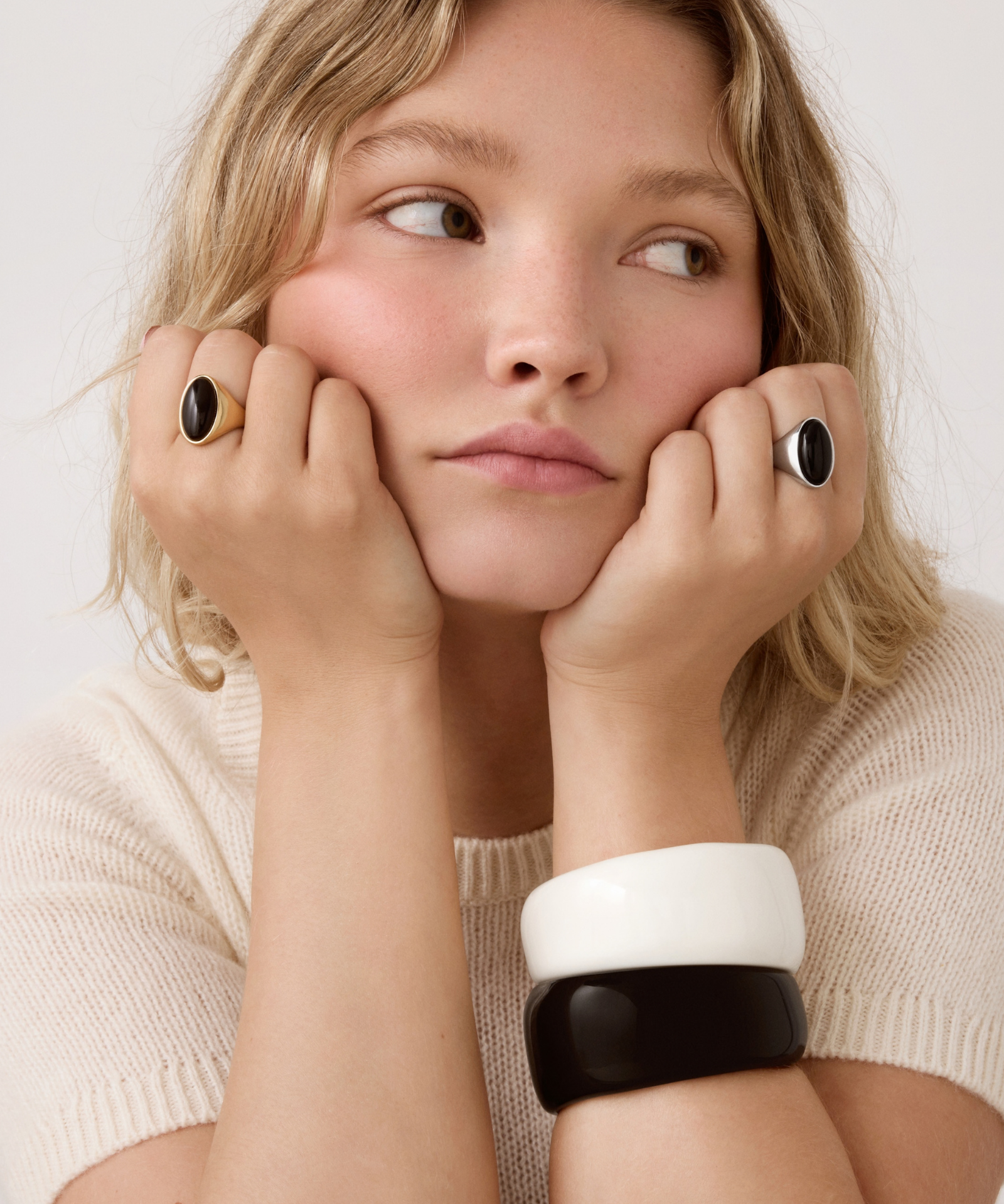 Close-up of model wearing gold and silver oval black stone rings with black and white cuff bracelets.