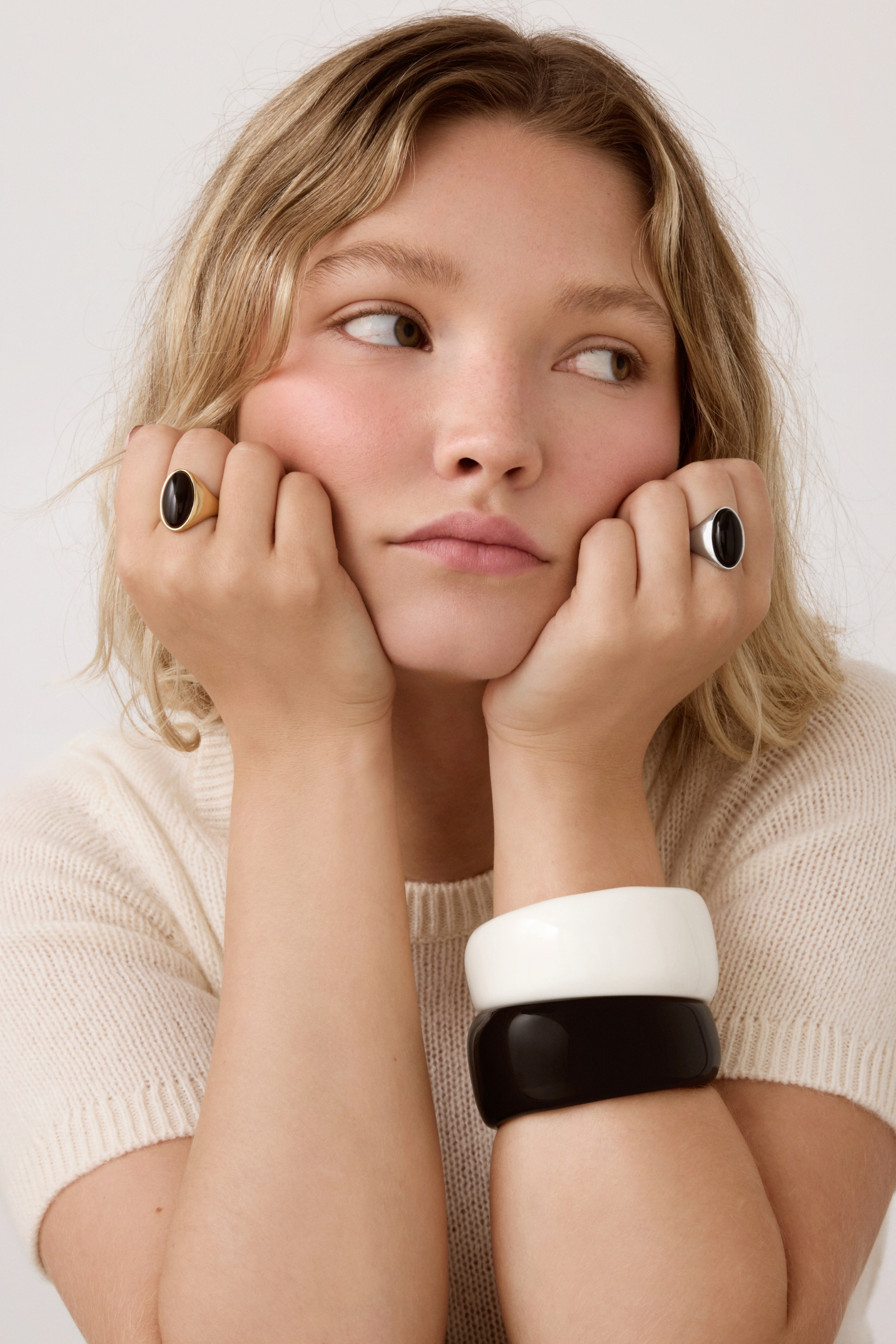 Close-up of model wearing gold and silver oval black stone rings with black and white cuff bracelets.