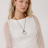 Model wearing a silver circular donut pendant cord necklace with matching silver huggie earrings.