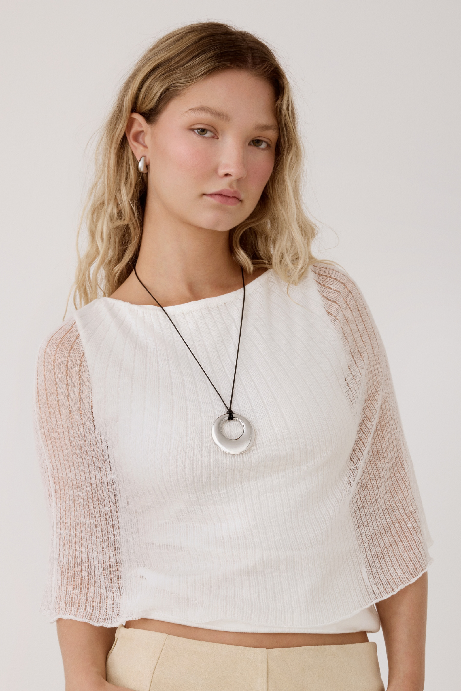 Model wearing a silver circular donut pendant cord necklace with matching silver huggie earrings.