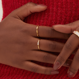 Close-up of a person in a red knit sweater, hands adorned with three gold rings. One ring has a small rectangular gem, another is the Alaska Ring in Gold Vermeil by Twenty Compass, and nails are neatly manicured.