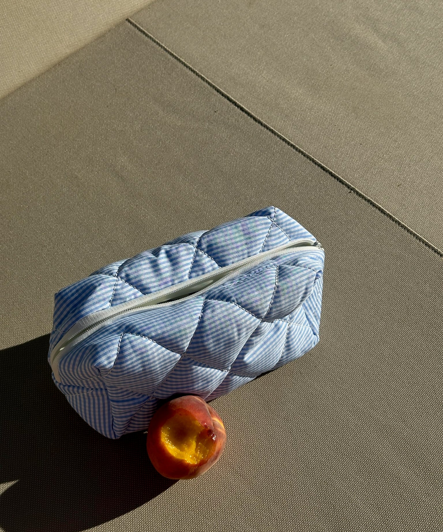 Twenty Compass Coastal Breeze Travel Pouch: A light blue and white striped, quilted travel pouch with a white zipper