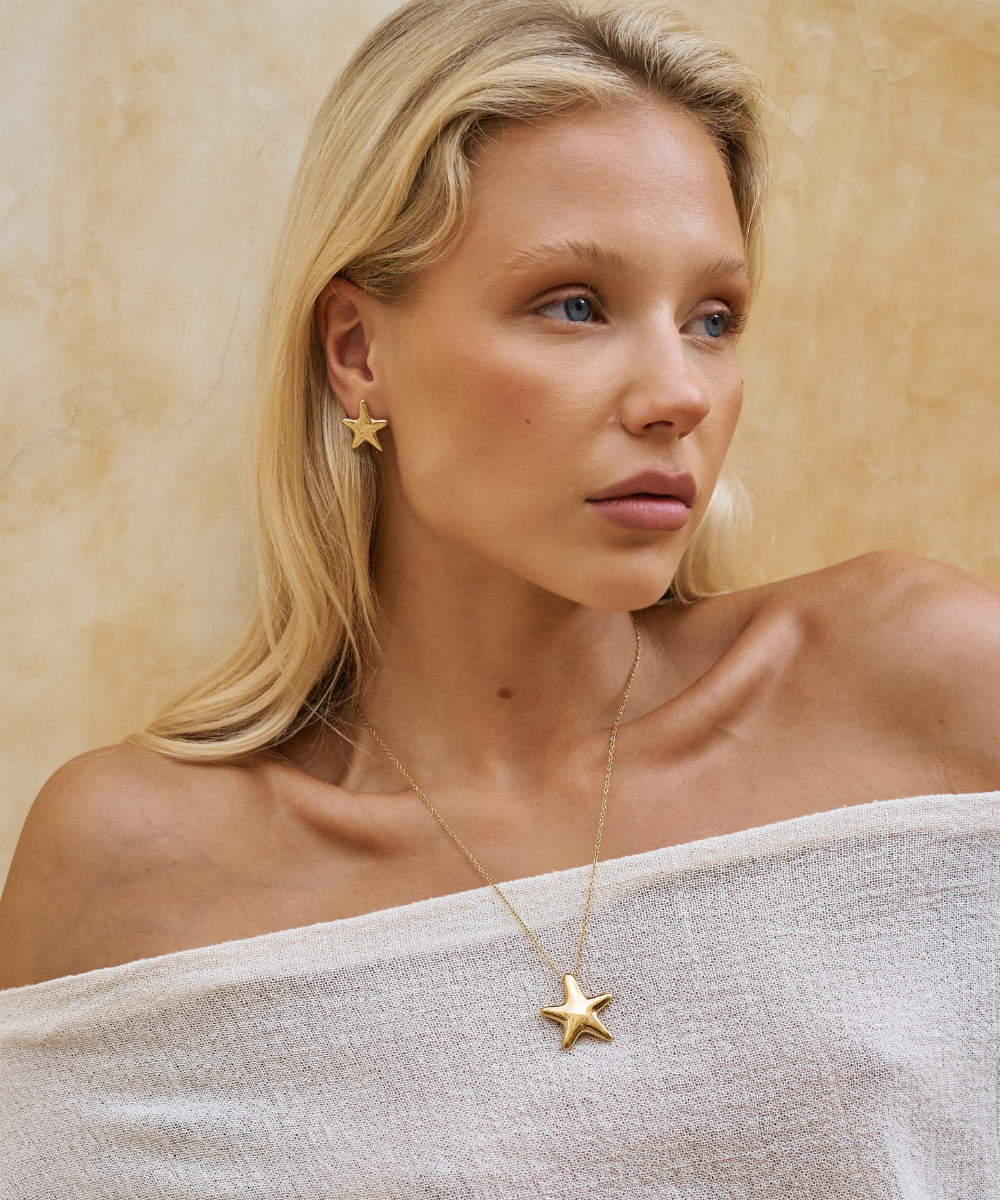 Woman wearing a gold star-shaped earring and necklace against a beige background