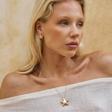Woman wearing a gold star-shaped earring and necklace against a beige background