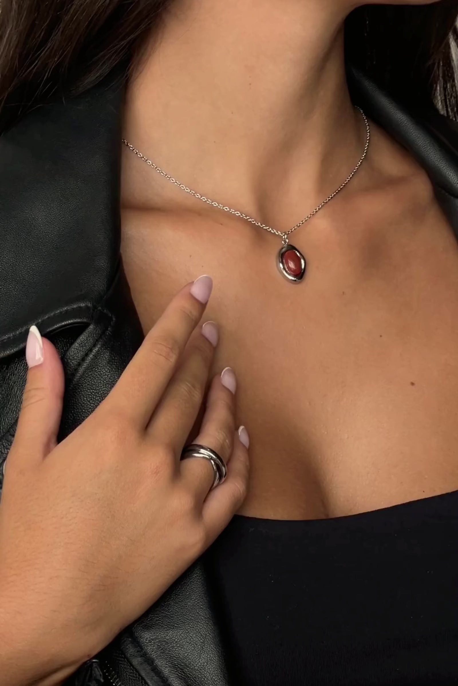 Video showcase of the Silver Bordeaux Necklace by Twenty Compass. The video features close-up shots of the organic-shaped Red Jasper stone pendant and the high-shine silver stainless steel chain. It demonstrates the adjustable 16 to 18-inch length and highlights the unique, natural variations in the deep red gemstone.