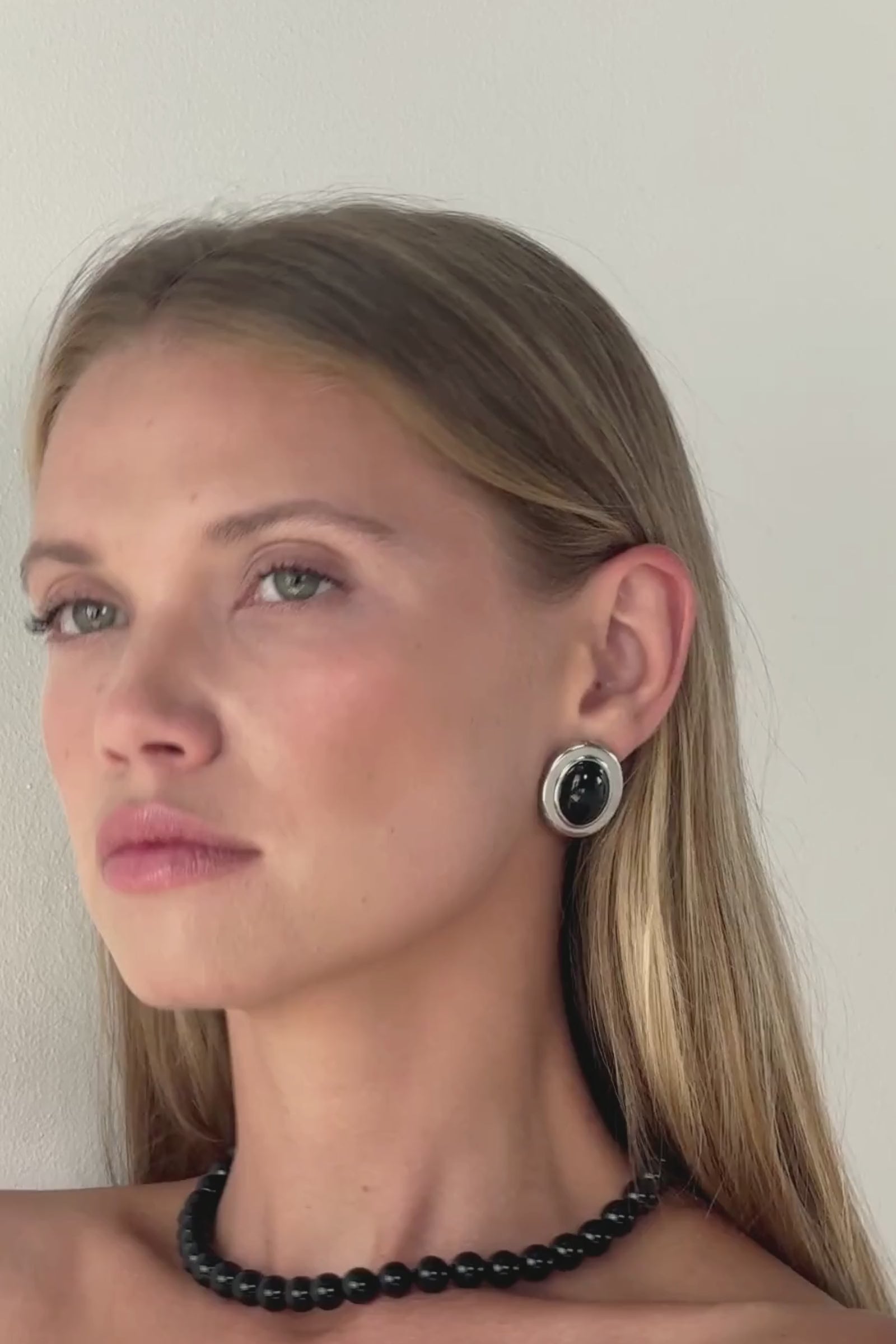 Video showcase of the Silver Velours Earrings by Twenty Compass. The video highlights the vintage-inspired oval stud design, featuring a smooth black enamel center framed by high-polish silver stainless steel. Close-up shots demonstrate the reflective quality and the durable, waterproof material of these '90s-style statement earrings.