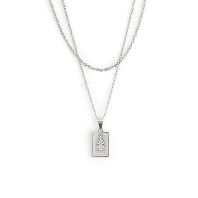 The Aparecida Necklace - Silver by TwentyCompass features a silver double-chain with a rectangular pendant engraved with the Virgin Mary in robes and the text APARECIDA on a white background, serving as a lucky charm.